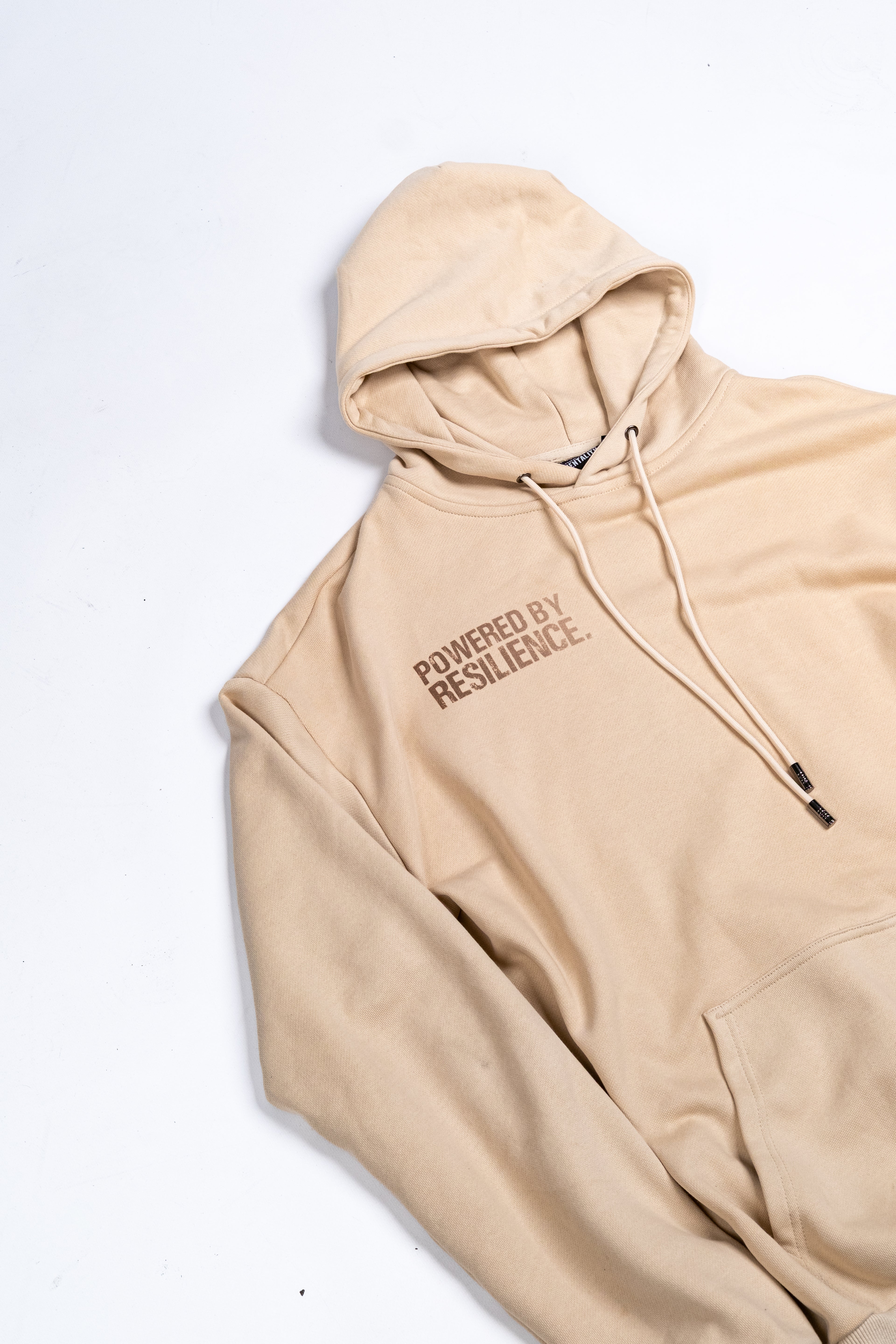 Beige Oversized Hoodie with brown gradient text saying powered by resilience. 100% premium cotton