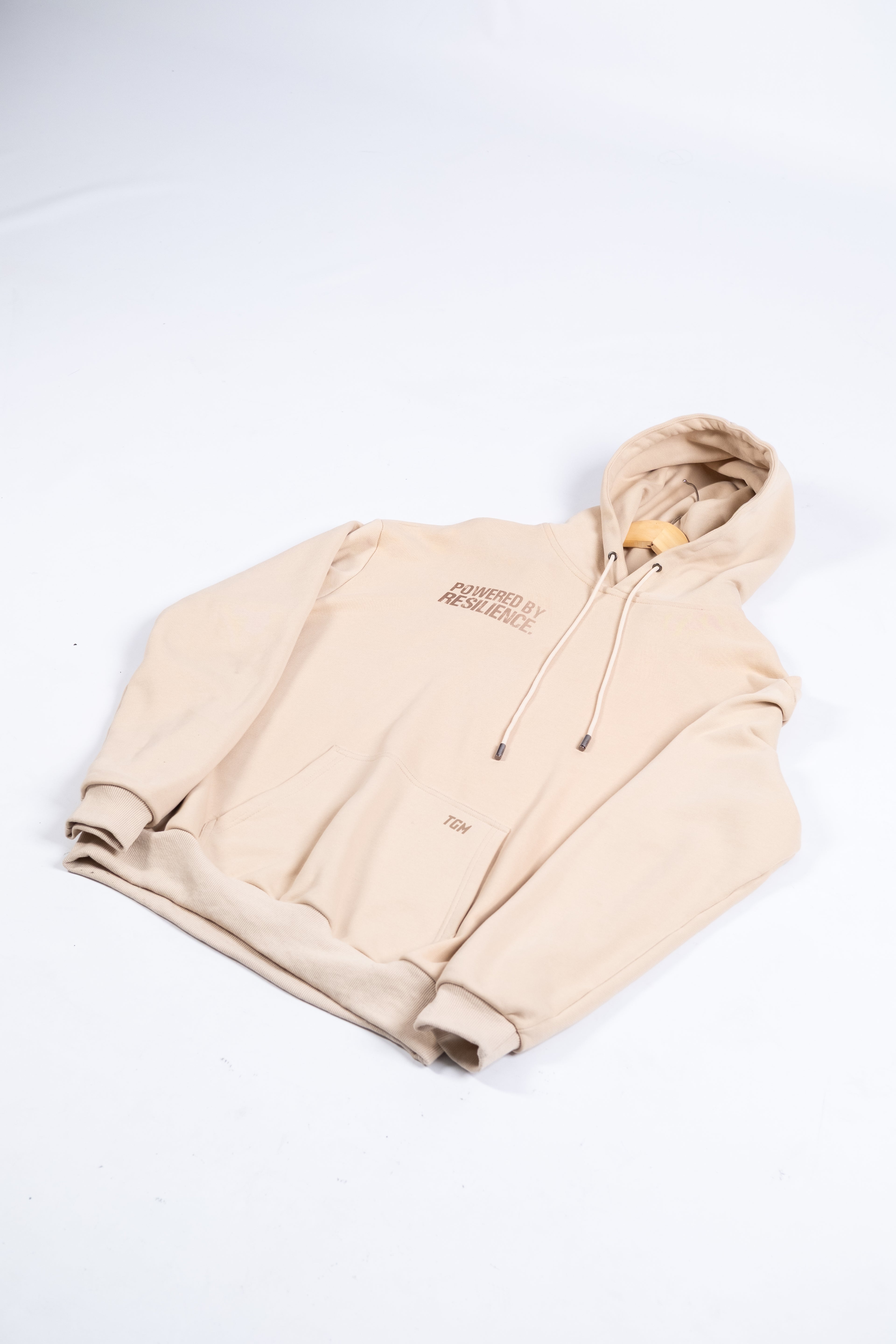 Beige Oversized Hoodie with brown gradient text saying powered by resilience. iso view 100% premium cotton